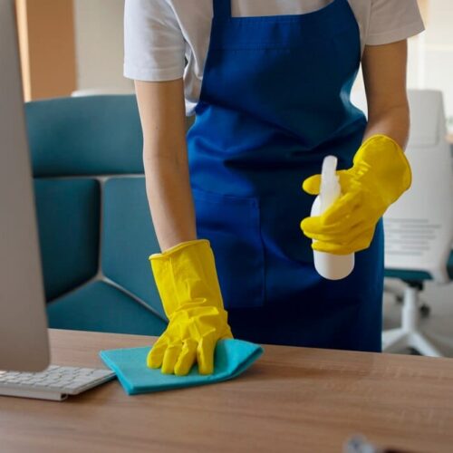professional-cleaning-service-person-cleaning-office_23-2150520628 (1) A woman in a blue apron providing house cleaning service at a desk.
